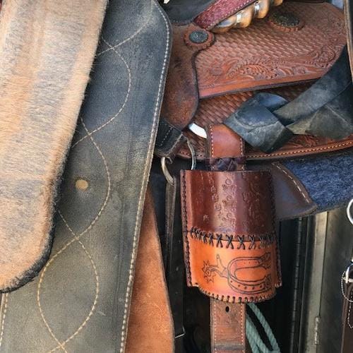 A leather bottle holder shown on the rear cinch of a saddle.