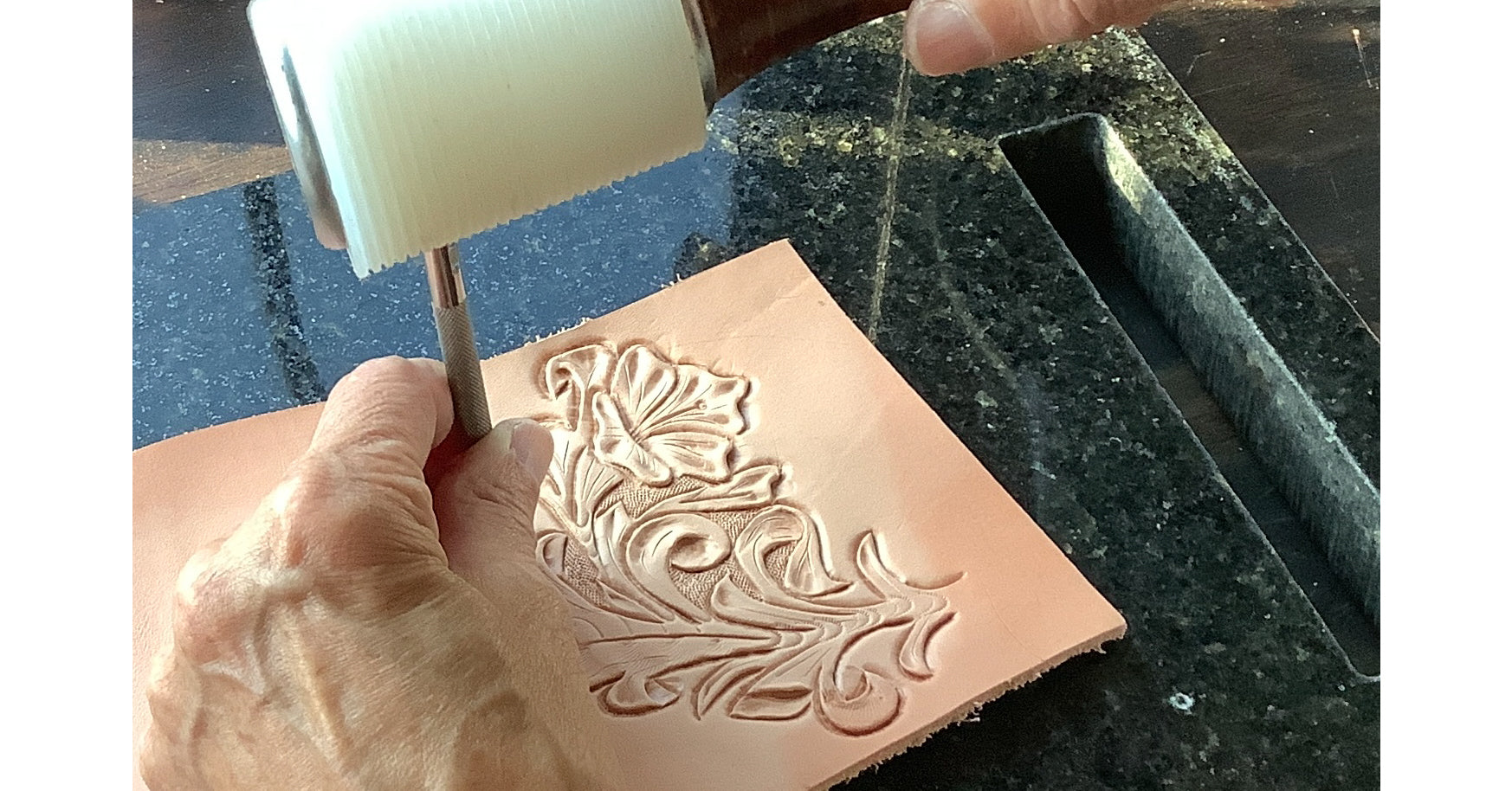 A person hand tooling a flower pattern on leather.