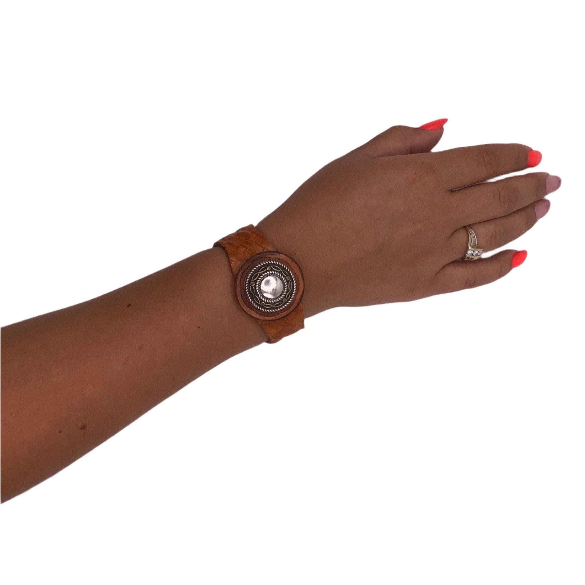Brown leather bracelet with a silver concho on a wrist against a white background