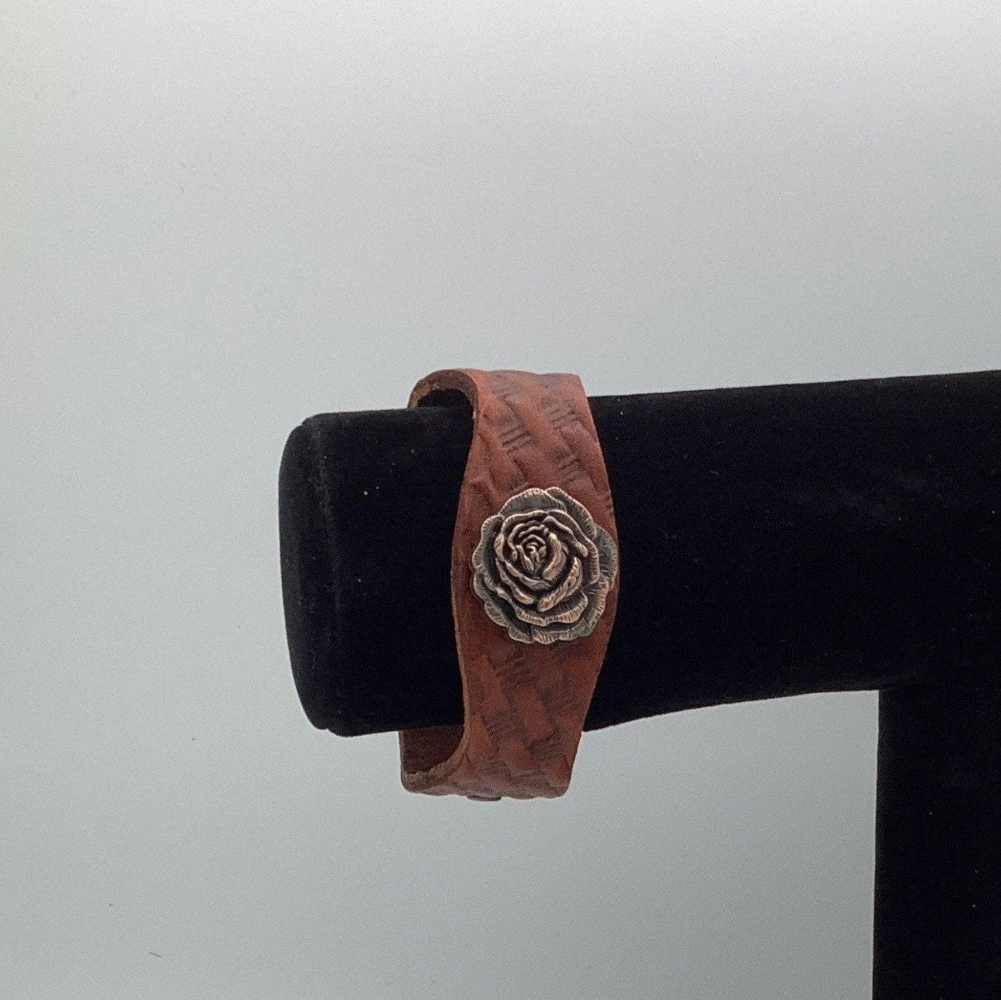 Brown leather bracelet with a copper rose concho on a black stand.
