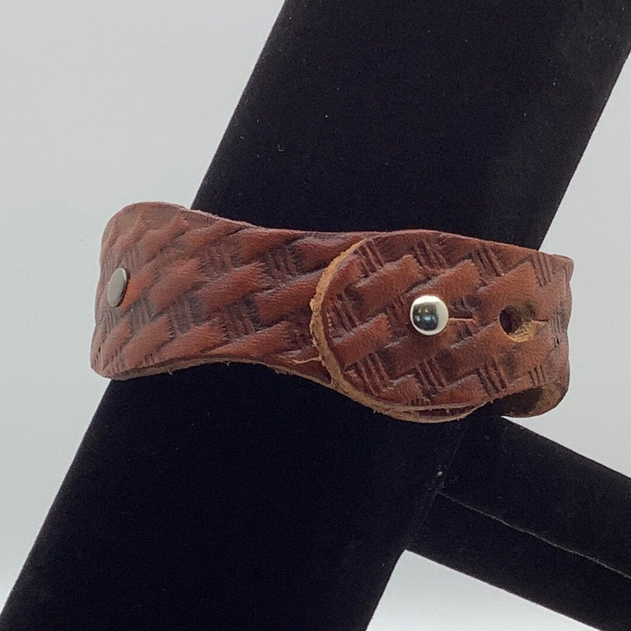 The clasp of a brown leather cuff bracelet on a black stand.