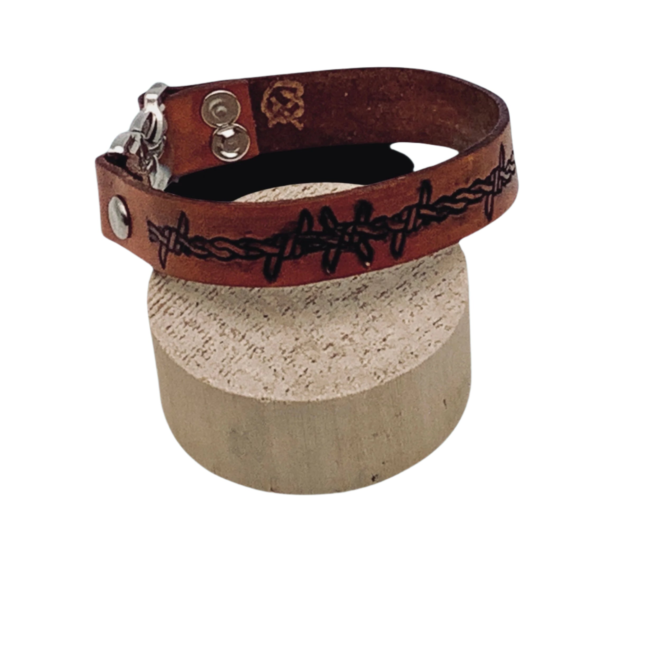 Brown leather bracelet with barbed wire design on a cylindrical block against a light blue background