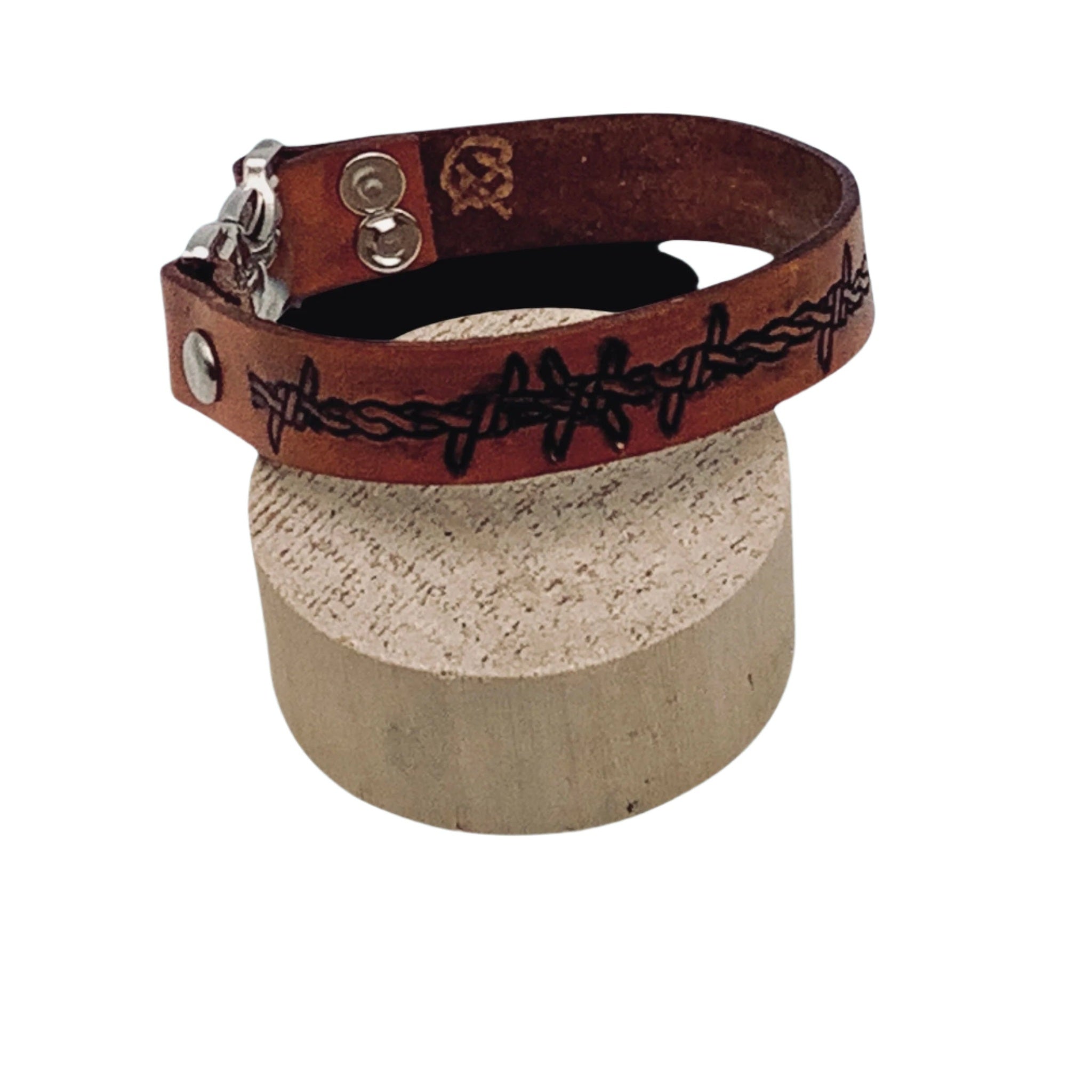 Brown leather bracelet with barbed wire design on a cylindrical block against a light blue background