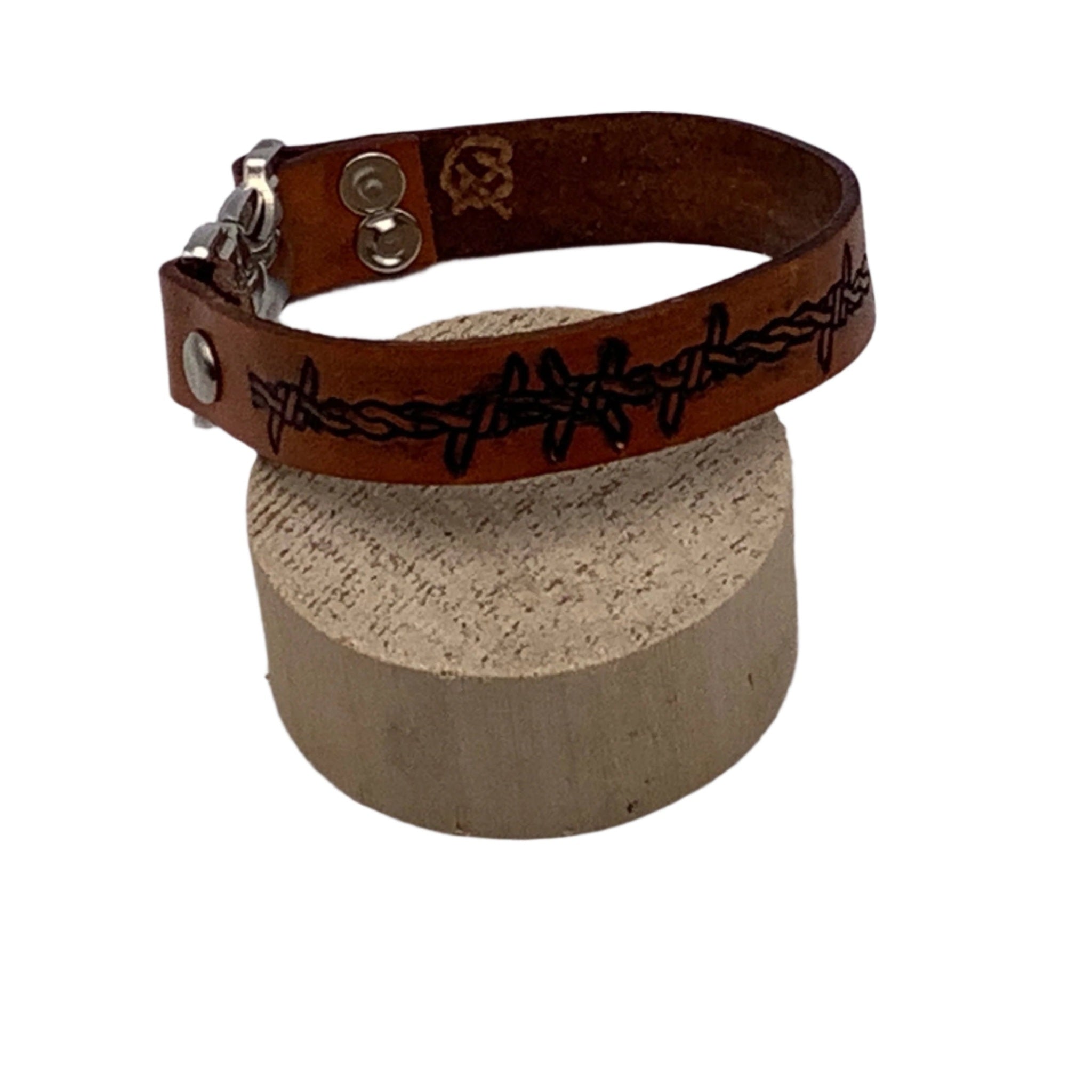 Brown leather bracelet with barbed wire design on a block against a white background