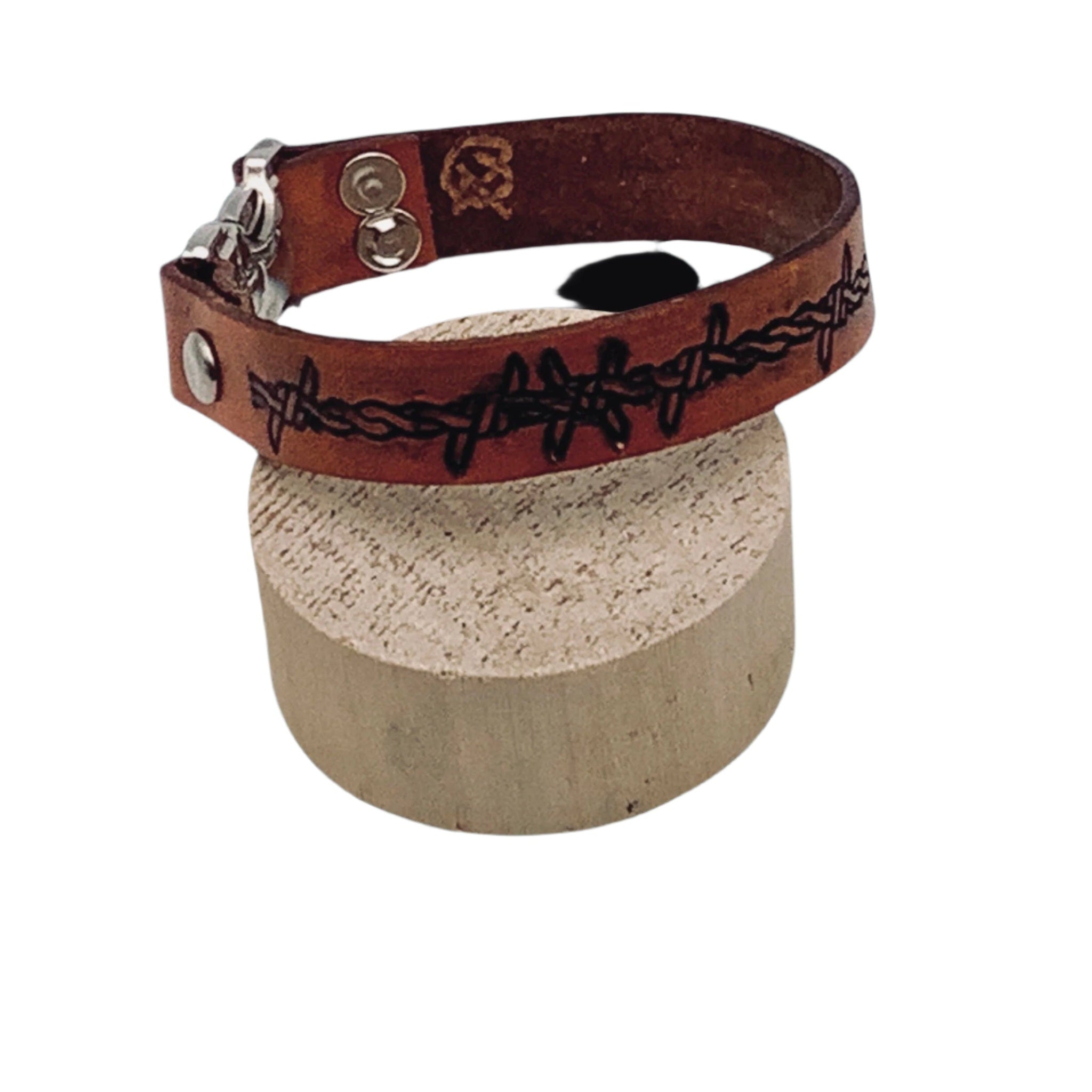 A close up of a brown leather bracelet with a silver clasp and a black barbed wire design.