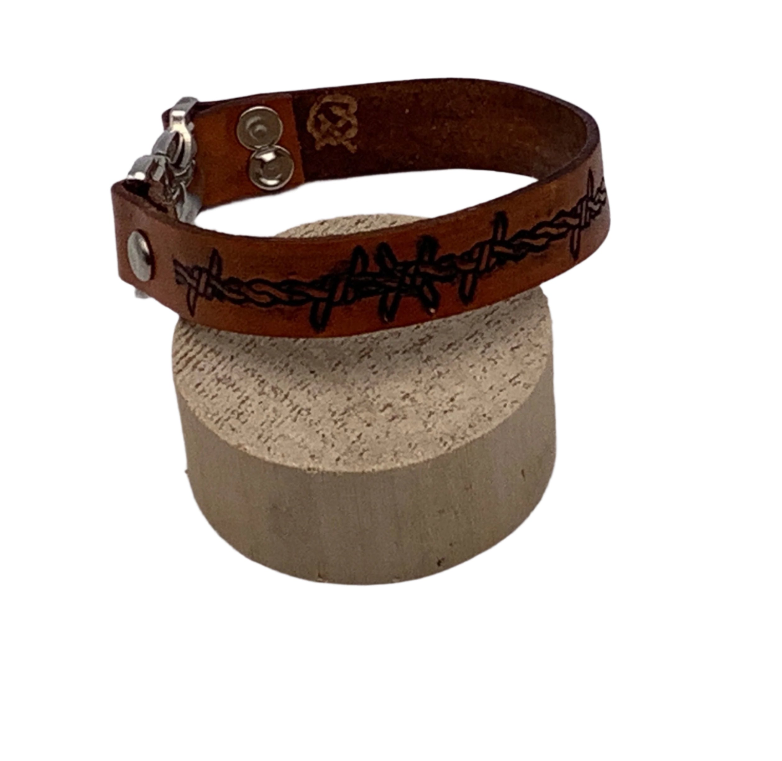 Brown leather bracelet with barbed wire design on a block against a white background