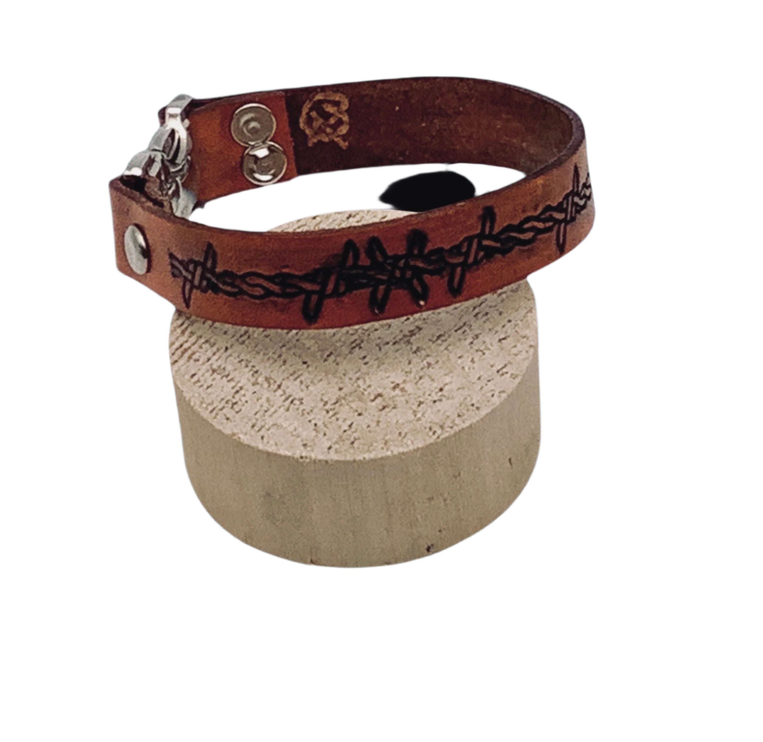 A close up of a brown leather bracelet with a silver clasp and a black barbed wire design.