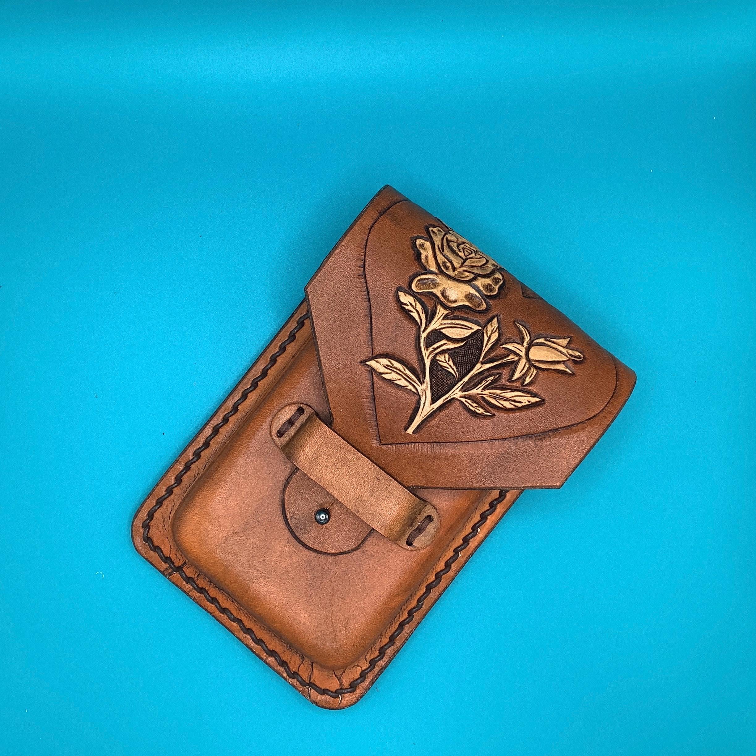A leather phone holder that attaches to a saddle billet with hand tooled roses inside a heart.