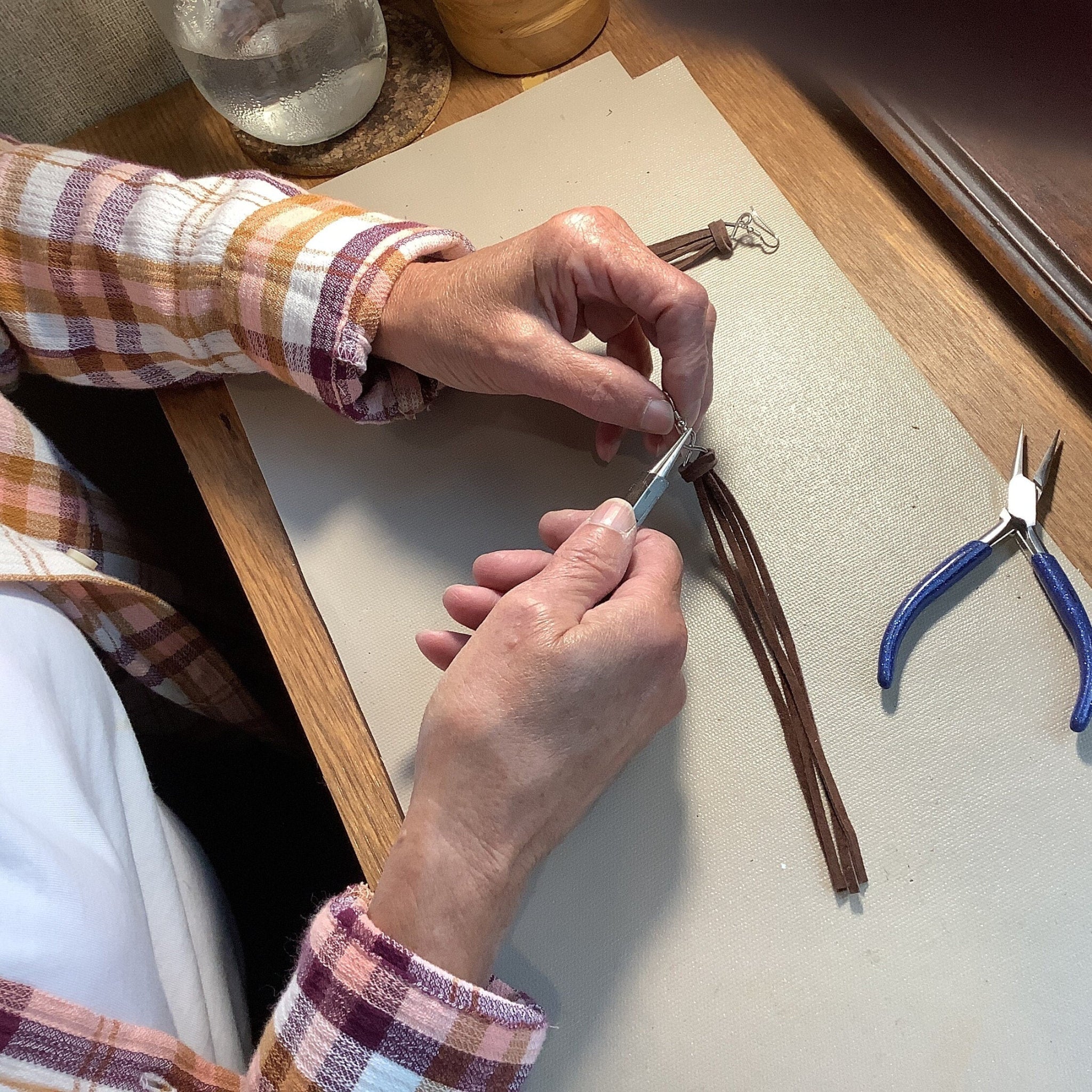 Leather worker crafting long brown leather lace earrings.