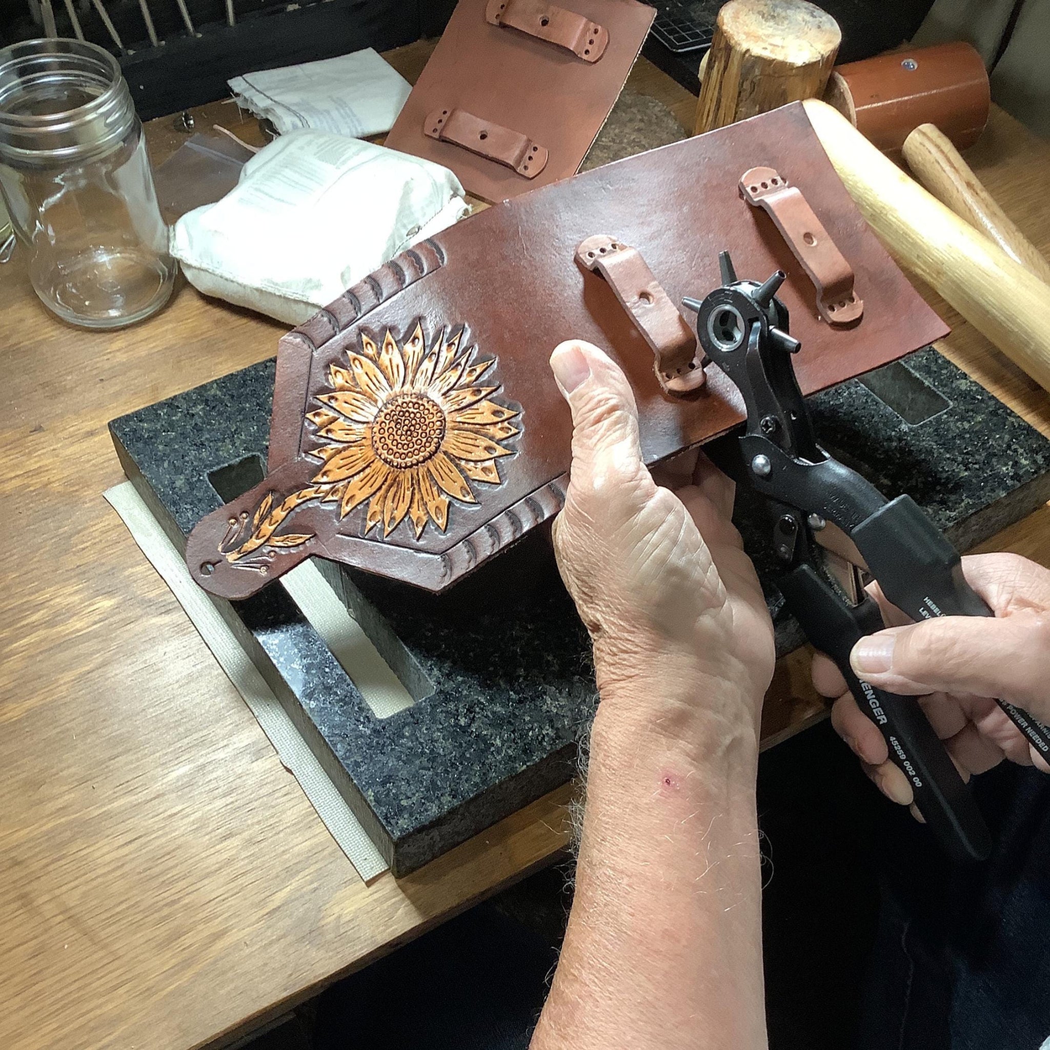 A leather worker crafting a sunflower phone holder for saddle.