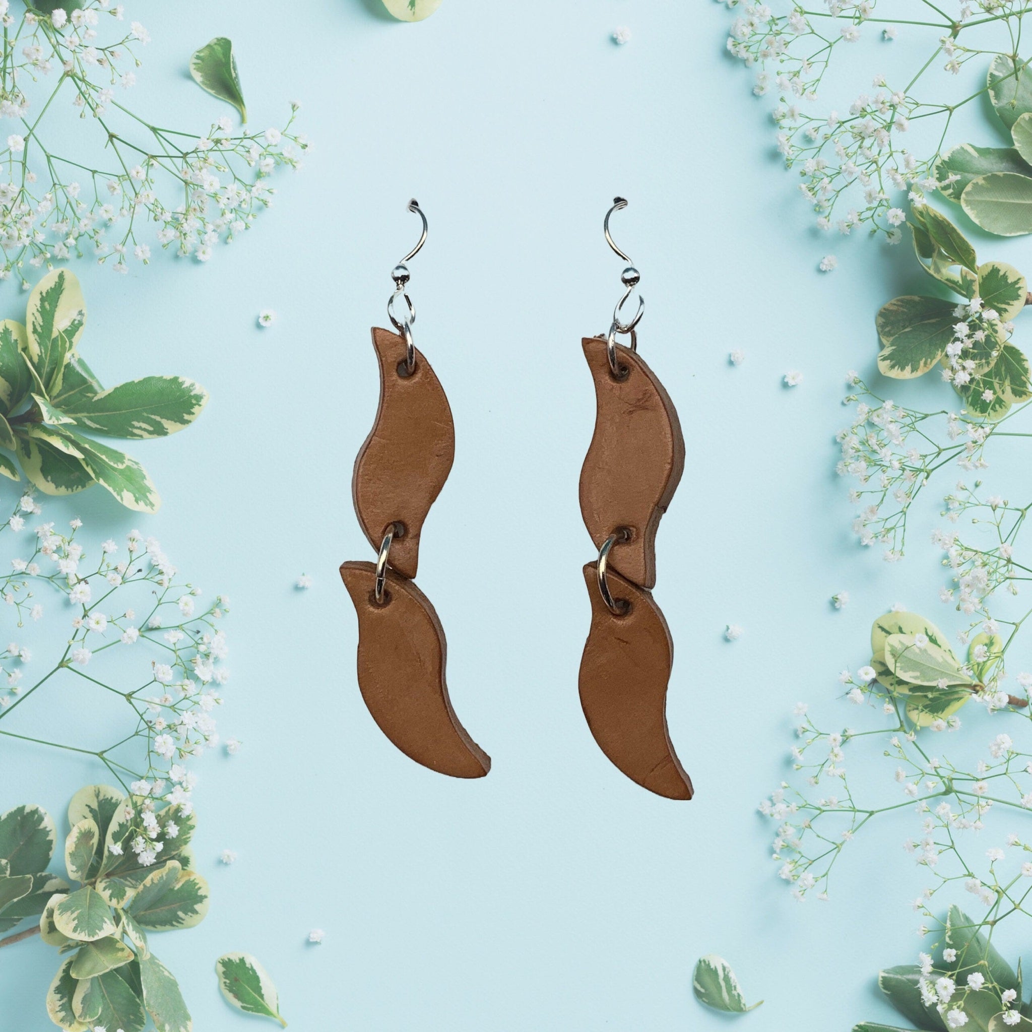 Long leather earrings on sterling silver ear wires shown on a flower background. 