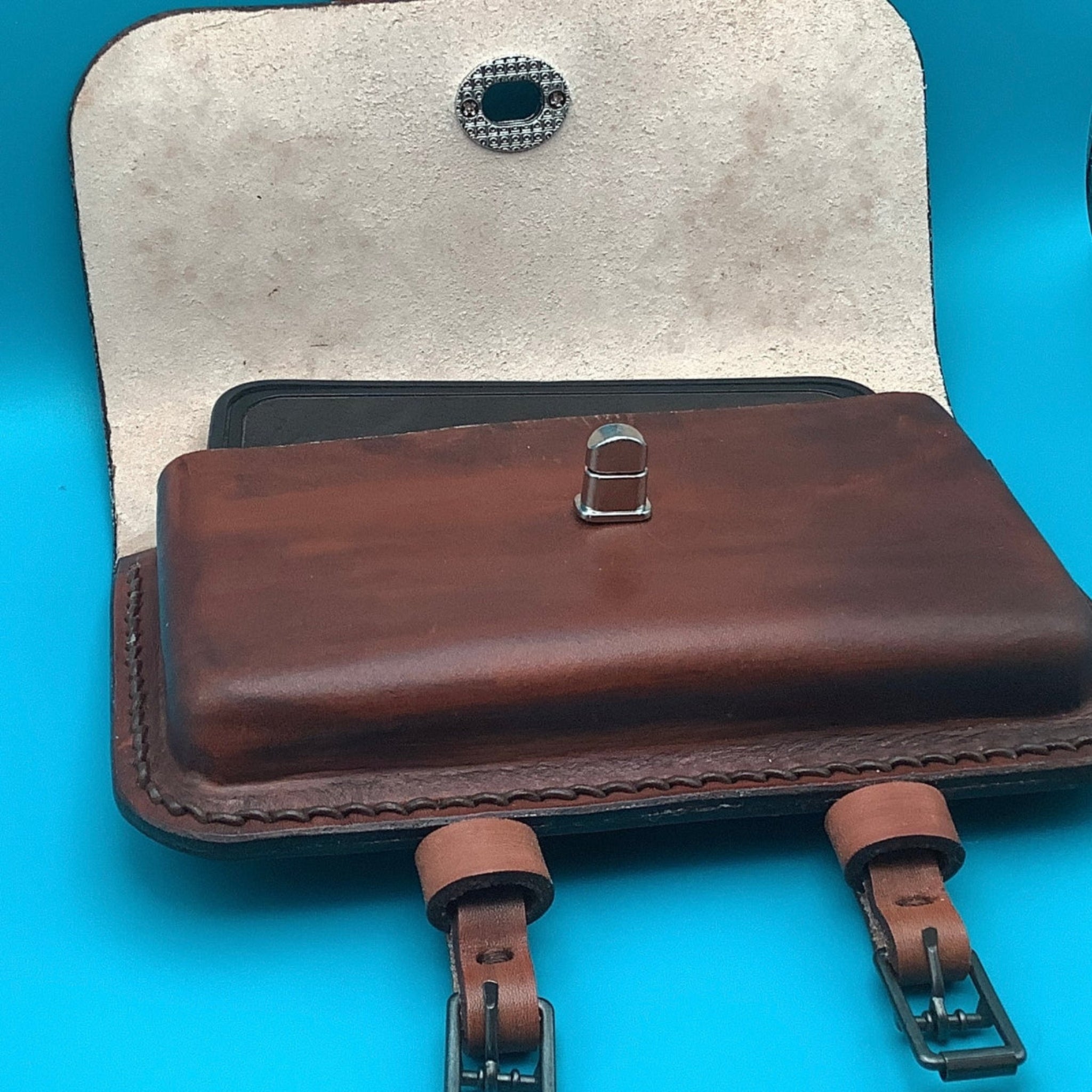 A mahogany leather horn bag with a cellphone in it.