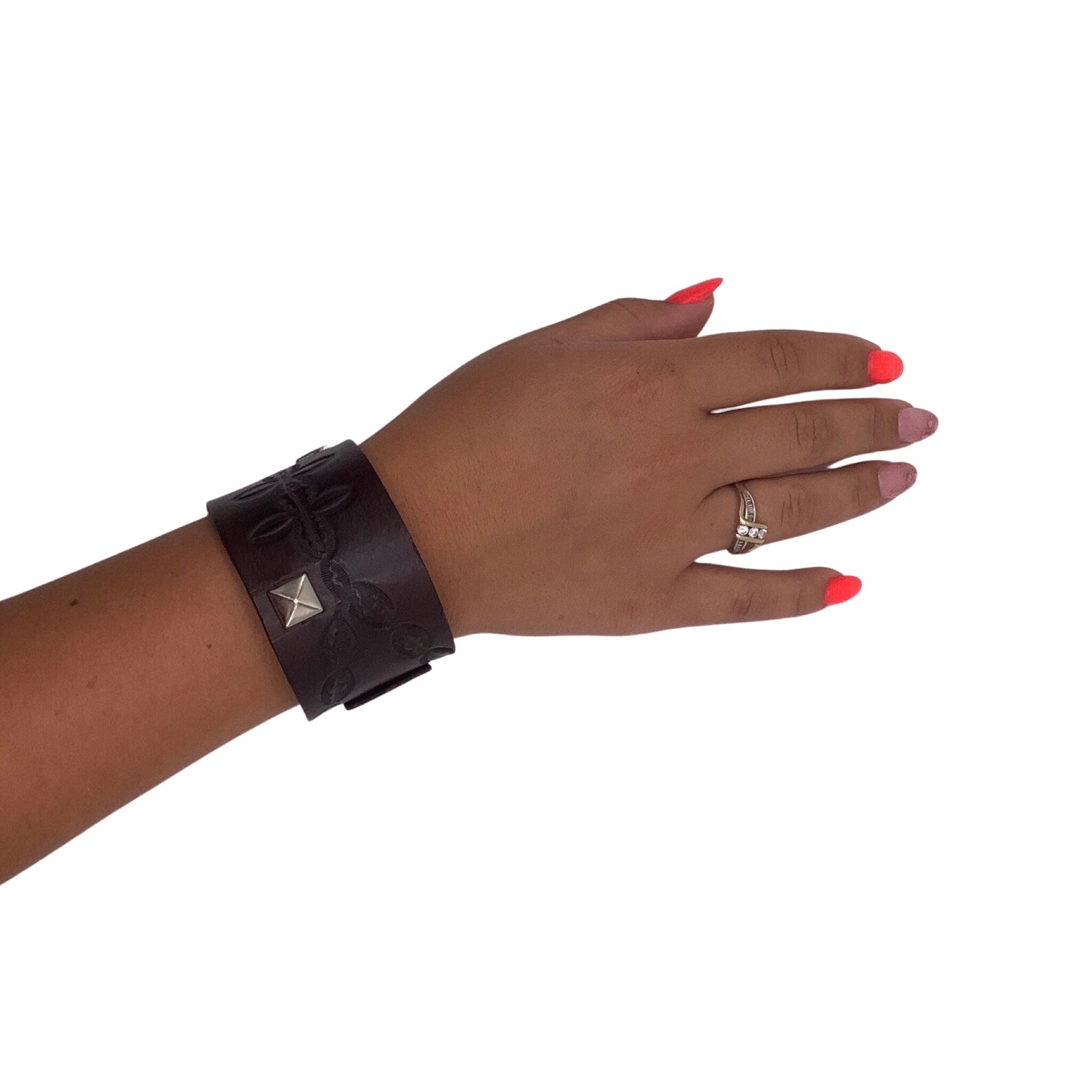 Wide leather bracelet with studs shown on a woman's hand.